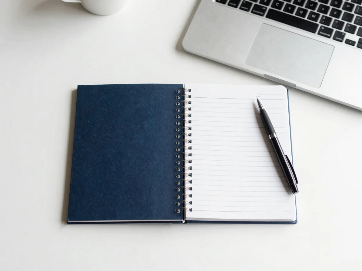Flatlay of an open application notebook with a pen and a laptop o